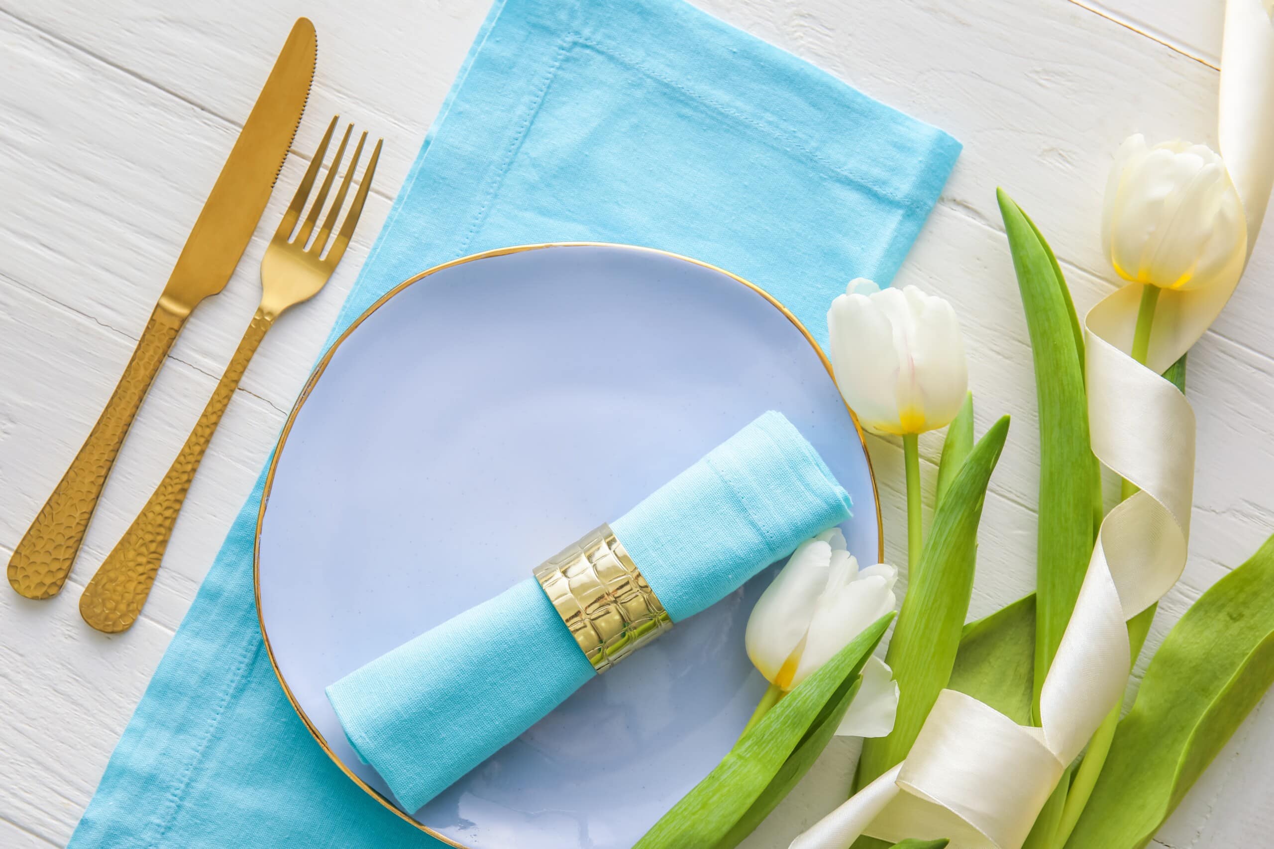beautiful place setting with blue napkin and plate and white tulips wrapped in ribbon