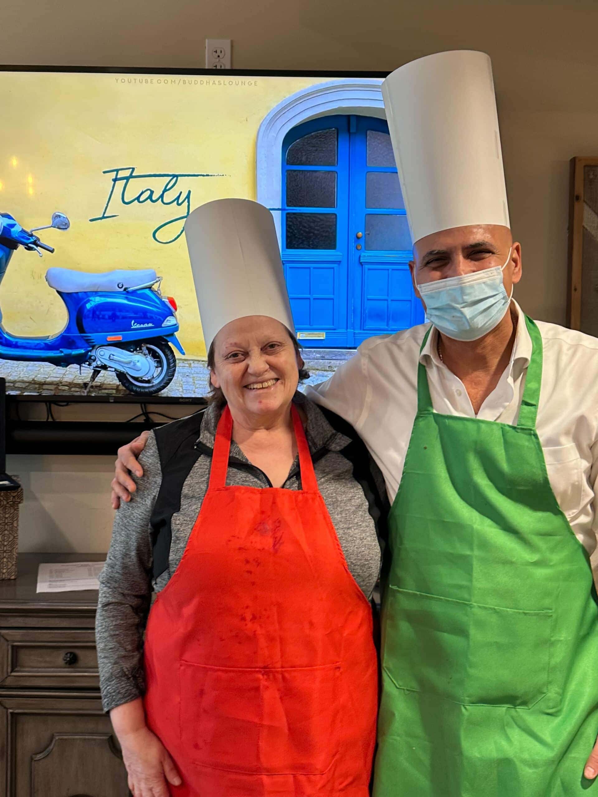 two adults standing with paper chef hats and aprons