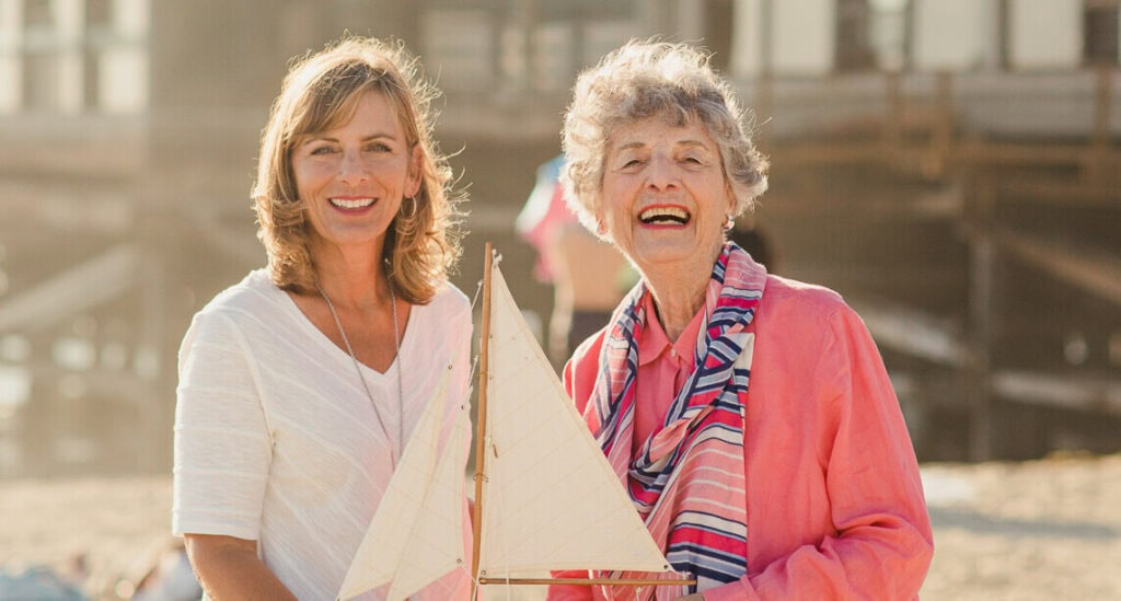 adult woman and elderly woman smiling holding small model sailboat
