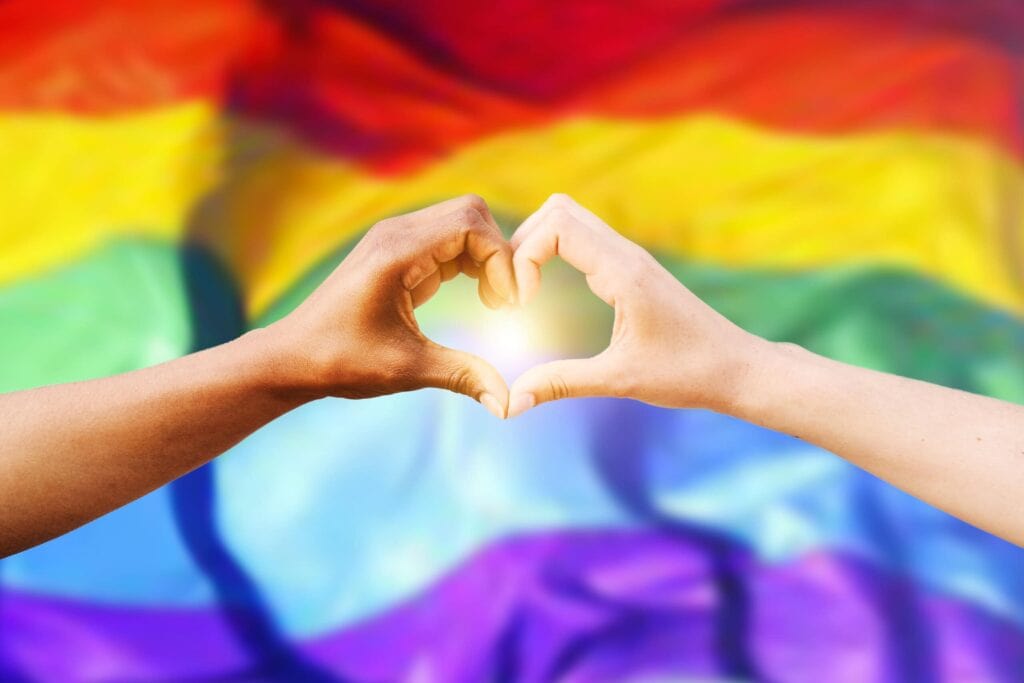 two hands making heart sign in front of rainbow flag