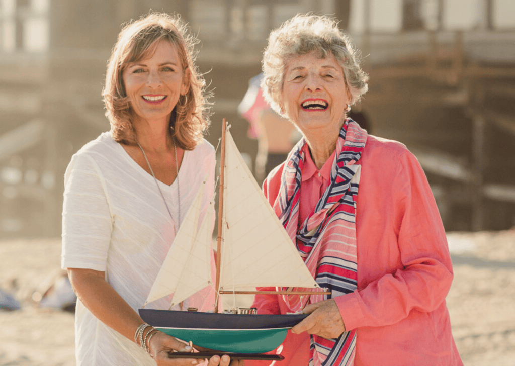 adult woman and elderly woman smiling holding small model sailboat