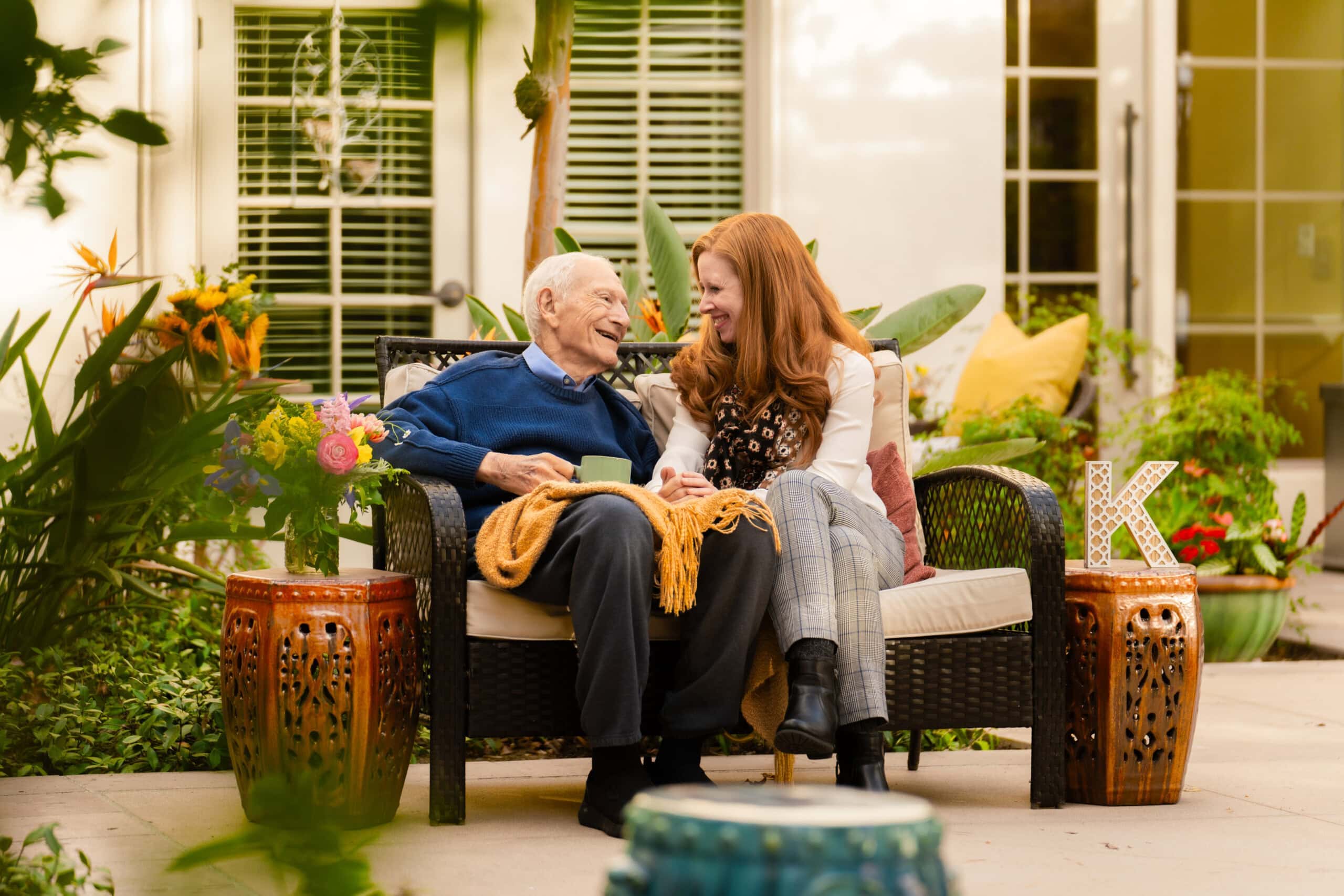 elderly man and woman sitting on bench and smiling at one another
