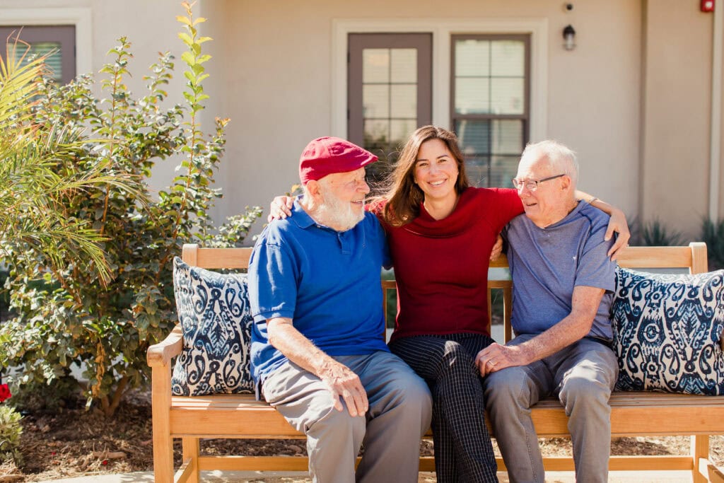 Three elderly people sitting on a bench outside.