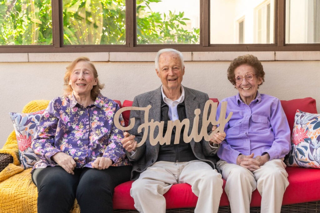 older man sitting between older ladies on bench holding sign that says family