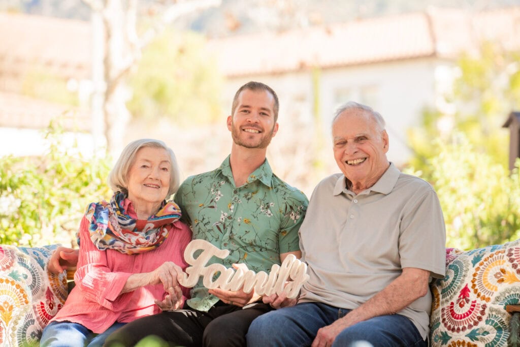 old couple and young man holding sign that says family