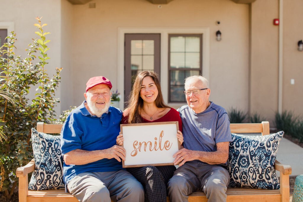 two old men with woman holding sign that says smile