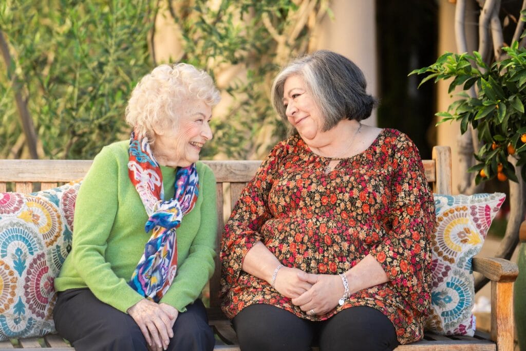 two ladies sitting on a bench and smiling together
